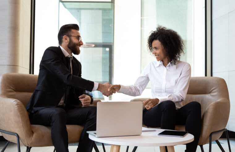 Image of two people shaking hands, sitting in front of a laptop